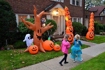 Two trick-or-treaters walking past a yard with Halloweens inflatable yard decorations.