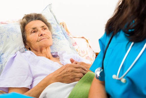 Elderly woman lays in bed with pain from bedsores caused by nursing home neglect.