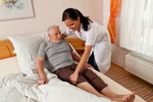 Nurse help elderly man into his bed at the nursing home.