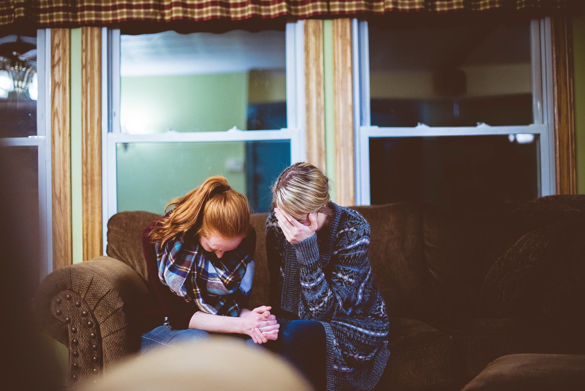 Two women sit on a couch sobbing from emotional distress.