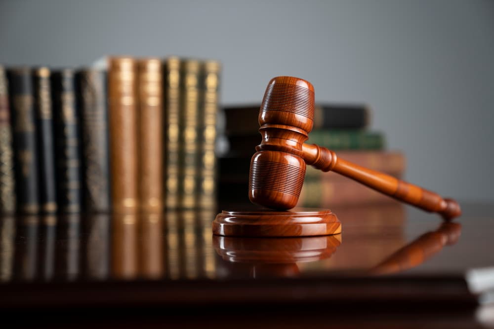 Wooden judge's gavel and striking block on a reflective desk in front of stacked law books, illustrating the procedural maintenance and adherence to rules during a personal injury lawsuit.